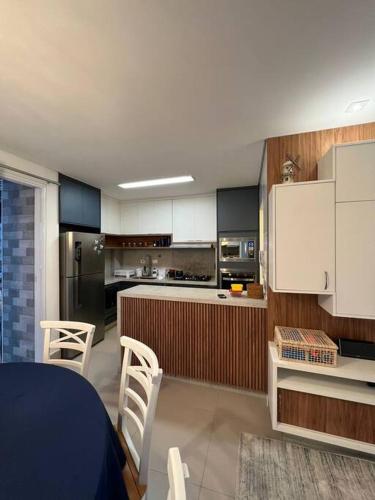 a kitchen with white cabinets and a blue table and chairs at Condomínio pé na areia, super novo e confortável. in São Sebastião