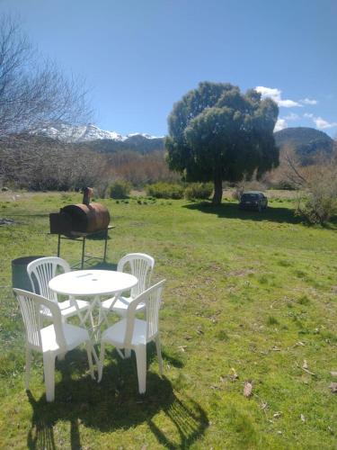 two white chairs and a table in a field at Cabaña de CAMPO Altos del Futaleufu sobre COSTA DE RÍO in Trevelin