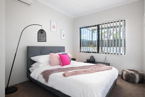 een witte slaapkamer met een groot bed met roze kussens bij U7/560 Cozy Lovely in Perth