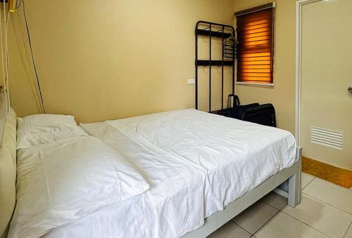a bedroom with a bed with white sheets and a suitcase at RedDoorz @ CMS Apartelle Olongapo City in Olongapo