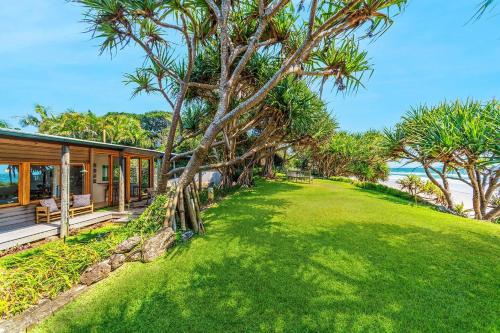 a house with a grass yard next to the ocean at Fuller Holidays - Belongil Beachside Cottage in Byron Bay