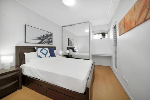 a white bedroom with a bed and a mirror at Trilogy Residences Brisbane in Brisbane