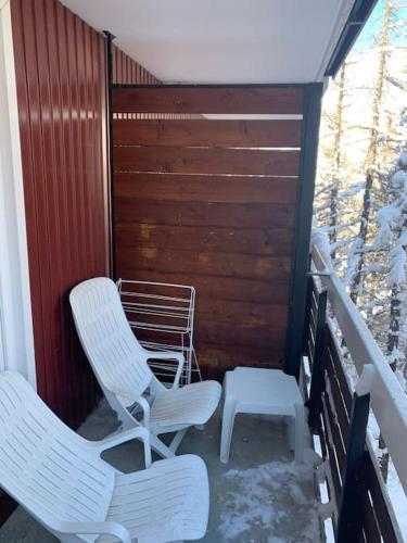 2 Stühle und ein Hocker auf einer Veranda in der Unterkunft Studio Le flocon in Vars