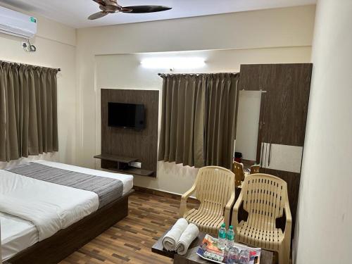 a bedroom with a bed and two chairs and a television at Hotel JP Grand in Bangalore