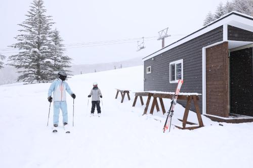 dos personas esquiando en la nieve cerca de una cabaña en Hotel Japan Shiga en Yamanouchi