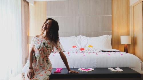 a woman in a dress standing next to a bed at Hotel Suni Sentani - Managed by East Season in Jayapura