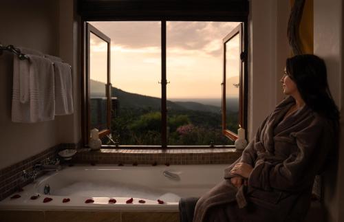 a woman sitting in a bath tub looking out a window at Kuzuko Lodge in Addo
