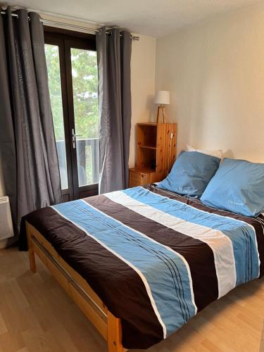 sypialnia z łóżkiem z niebieskimi poduszkami i oknem w obiekcie Plein Sud w mieście Eygliers