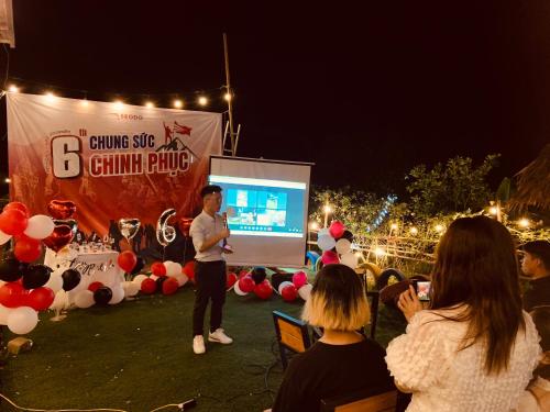 Ein Mann steht auf einem Bildschirm vor einer Menge in der Unterkunft Nhà Gỗ An Trăm Tuổi - Chill Garden Lakeview in Hanoi