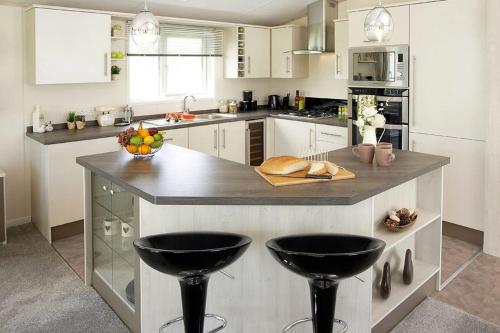 a kitchen with a large island with two black bar stools at Newperran Holiday Park in Newquay