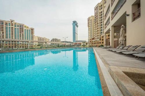 a large blue swimming pool with chairs and buildings at Sunset Lake Condo - RP Home in Dubai