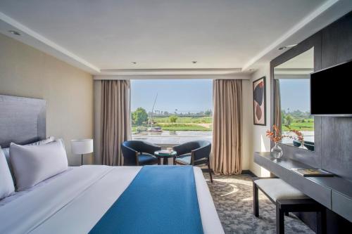 a hotel room with a bed and a large window at Mövenpick Royal Lily Monday Four Nights Luxor Friday Three Nights Aswan in Luxor