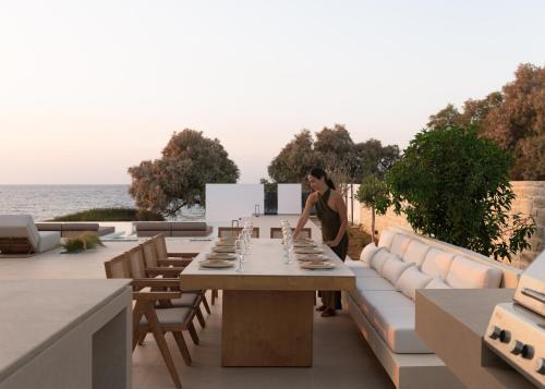 a woman standing next to a table on a patio at Asea Villa, Spectacular right-on-the-beach Retreat, By ThinkVilla in Skaleta