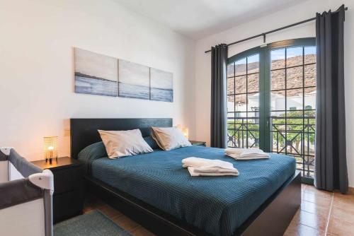 sypialnia z łóżkiem z niebieską pościelą i oknem w obiekcie Residencial Las Candelarias 34 w mieście Agaete