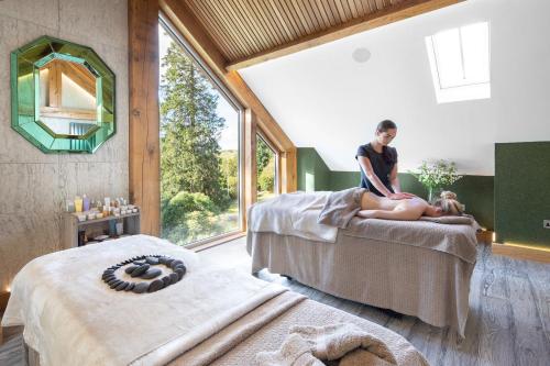 a woman sitting on a bed in a room with a window at Gilpin Hotel & Lake House in Bowness-on-Windermere