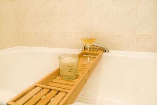 a wooden tray with a glass and a wine glass on a bath tub at Longbridge Apartment- 1BR Close to Gatwick in Hookwood
