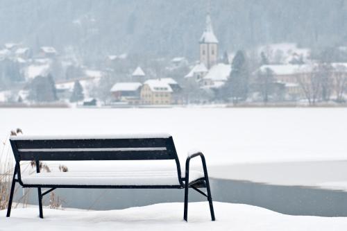 a bench sitting in the snow next to a body of water at Waldvilla BERGSEE in Bodensdorf