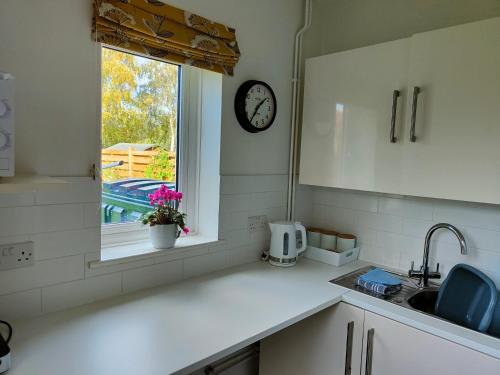 eine Küche mit einem Waschbecken und einer Uhr am Fenster in der Unterkunft Self contained annexe in pretty Suffolk village in Bury Saint Edmunds