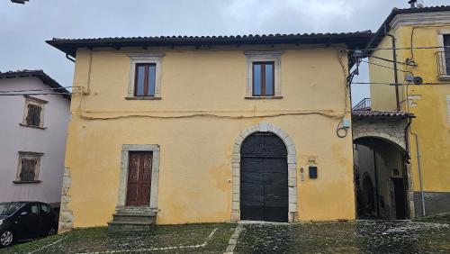 an old yellow house with a black door and windows at Appartamento La Locanda Del Castello in San Panfilo dʼOcre