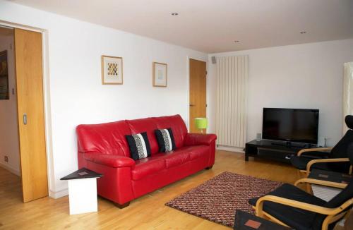 sala de estar con sofá rojo y TV de pantalla plana en JOIVY Inviting flat with parking in Canonmills, en Edimburgo