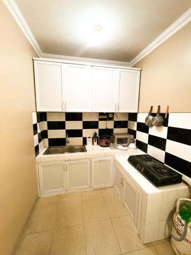 uma cozinha com armários brancos e azulejos pretos e brancos em Homestay Kamar Tamu Godean em Godean