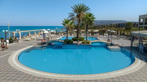 a large swimming pool with palm trees and the ocean at Hydramis Palace Beach Resort in Georgioupolis