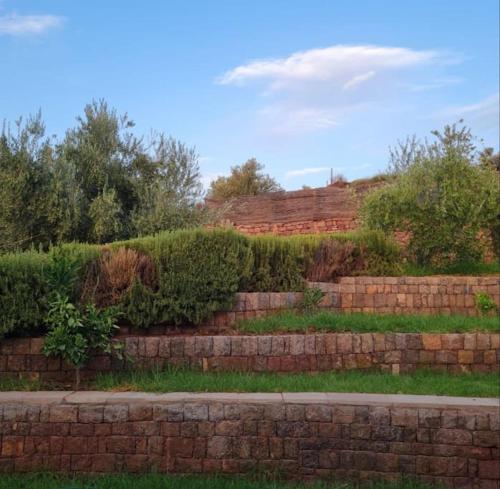 a brick retaining wall with bushes and trees at Le Figuier du Lac Bin elouidane in Bine el Ouidane