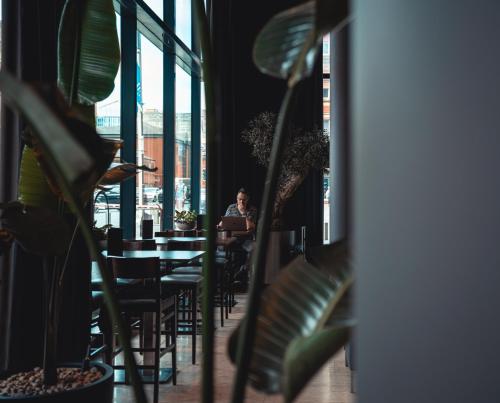 a man sitting at a table in a restaurant with plants at The Manchester Deansgate Hotel, by IHG in Manchester