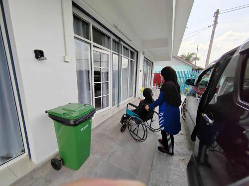 a woman with a child in a wheelchair next to a building at MKB Homestay - Landed Studio room with 2 Queen bed and Free gated Parking in Shah Alam