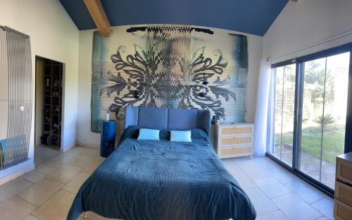 Un dormitorio con una cama azul con una pintura en la pared en Villa avec Pool House au cœur des vignes - Lubéron, en La Tour-dʼAigues