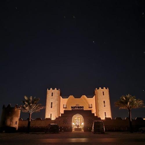 un bâtiment éclairé la nuit avec des voitures garées devant dans l'établissement Palms Garden, à Erfoud