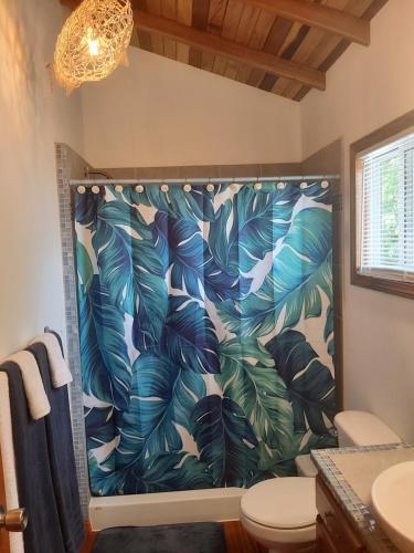 a bathroom with a shower curtain with tropical leaves at Bella Vita Casitas in Placencia