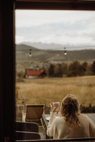 a woman holding a cup of coffee looking out of a window at Loft&Hill in Grywałd