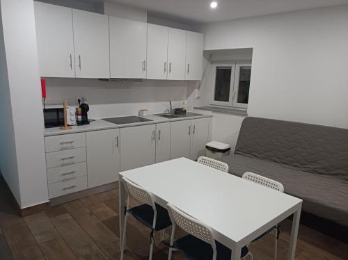 a kitchen with white cabinets and a table and a bed at Casa Amado Fundão in Fundão