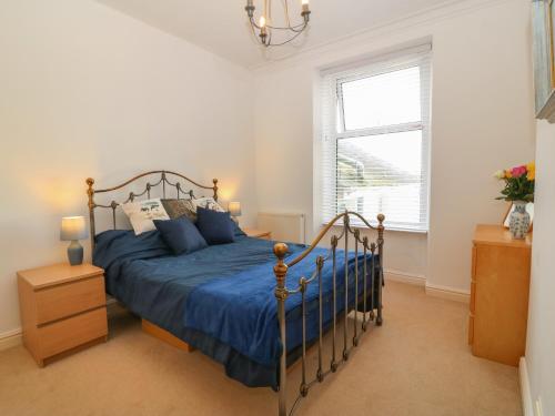 a bedroom with a bed with blue sheets and a window at Tonnau Waves in Pwllheli