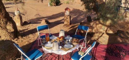 a table and chairs on the beach with a table and chairs at Camp M'hamid Ras N'khal in Mhamid