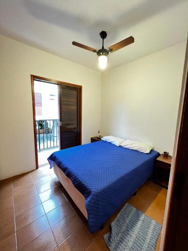 um quarto com uma cama azul e uma ventoinha de tecto em Apê Itaguá - CentrinhoTurístico de Ubatuba em Ubatuba