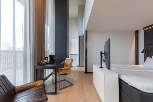 a bedroom with a bed and a desk with a television at Leonardo Hotel Groningen in Groningen