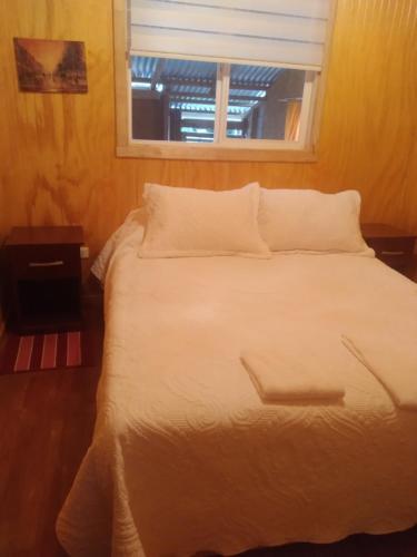 ein weißes Bett mit Fenster in einem Zimmer in der Unterkunft Cabaña carmencita in Puerto Puyuhuapi