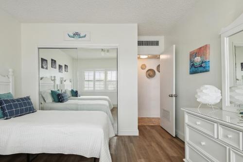 a white bedroom with two beds and a mirror at Sunrise at the Beach - 2BR Apt with Scenic Views in Satellite Beach