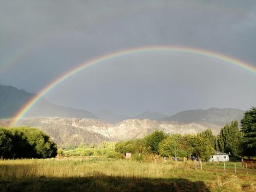 a rainbow over a field with mountains in the background at Rincón Bonito in El Hoyo