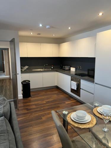 Stunning Manchester City Centre Apartment! Ideal for small groups في مانشستر: مطبخ مع طاولة طعام ومطبخ مع دواليب بيضاء