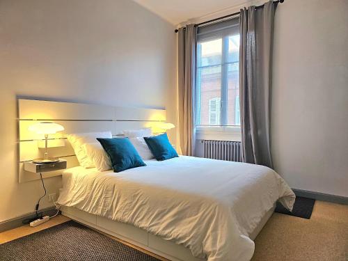 a bedroom with a bed with blue pillows and a window at L'Idrac, Appartements en Hyper centre in Toulouse