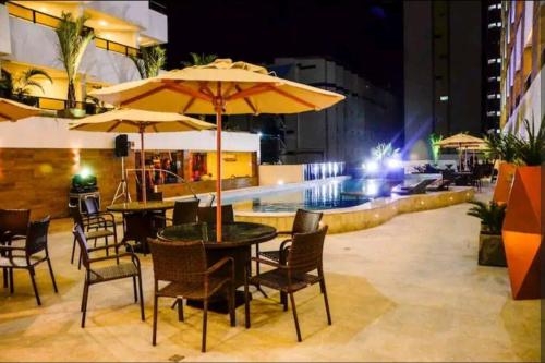 a table and chairs with umbrellas next to a pool at Flat a 50m da beira-mar do Cabo Branco - Gold Flat 121 in João Pessoa