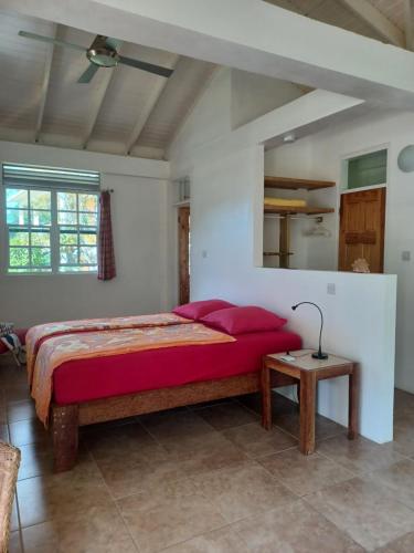 Schlafzimmer mit einem Bett mit roten Kissen und einem Tisch in der Unterkunft Mango Garden Cottages in Tanetane