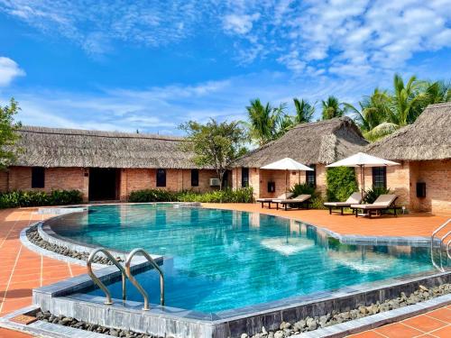 a pool at a resort with thatched huts at ENSO Retreat Hoi An in Hoi An