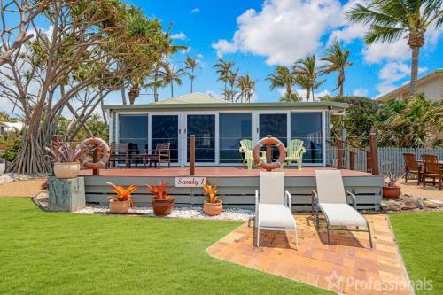 a house with chairs and a patio with palm trees at Beachfront Holiday Cottage in Zilzie