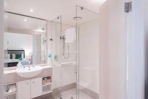 Un baño blanco con lavabo y ducha. en Azure Harmony - A Breezy Hideaway at The Beach Club, en Palm Cove