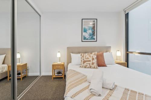 a bedroom with a large white bed and a mirror at Light Filled 2BR Apt with Balcony, Parking, Cafes & Restaurants in Melbourne
