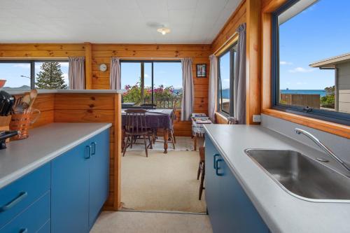 une cuisine avec des placards bleus et une salle à manger avec une table dans l'établissement Bay View Bach - Langs Beach Holiday Home, à Waipu